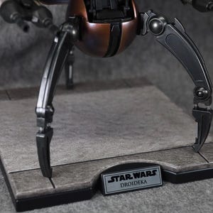 Puede incluir: Modelo detallado de un Droideka de Star Wars, un droide destructor rodante. El modelo presenta una combinaci&oacute;n de colores marr&oacute;n met&aacute;lico y negro, con patas articuladas y bl&aacute;sters. La base tiene una placa con el nombre Star Wars Droidika.