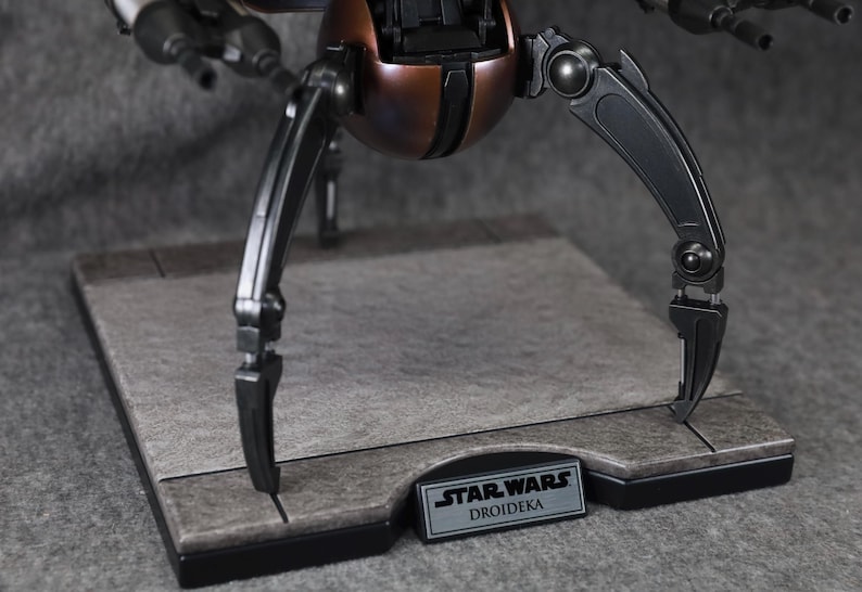 Puede incluir: Modelo detallado de un Droideka de Star Wars, un droide destructor rodante. El modelo presenta una combinaci&oacute;n de colores marr&oacute;n met&aacute;lico y negro, con patas articuladas y bl&aacute;sters. La base tiene una placa con el nombre Star Wars Droidika.