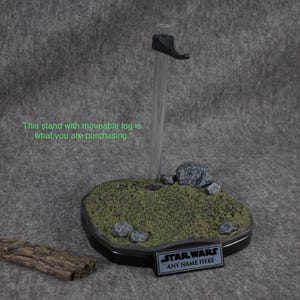 May include: A black plastic display stand with a removable log, rocks, and green foliage. The stand has a black plaque with the text "STAR WARS ANY NAME HERE".