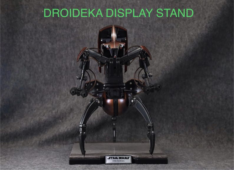Puede incluir: Un soporte de exhibici&oacute;n detallado para una figura de Droideka, con una combinaci&oacute;n de colores marr&oacute;n y negro met&aacute;lico. El soporte tiene un logotipo de Star Wars y el texto "DROIDEKA DISPLAY STAND" en verde.