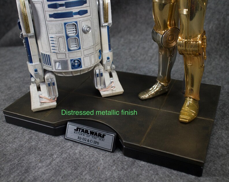 May include: A distressed metallic finish base with a silver plaque that reads "STAR WARS RETURN OF THE JEDI R2-D2 & C-3PO".  The base features a silver and gold robot figurine.