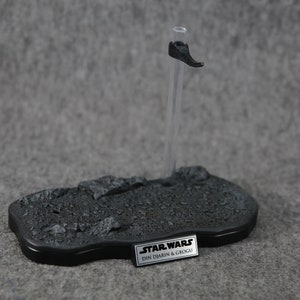 Puede incluir: Un soporte de exhibici&oacute;n negro para figuras de acci&oacute;n con una base texturizada y una varilla de soporte transparente. El soporte presenta un peque&ntilde;o reposapi&eacute;s negro y una placa rectangular con el texto "STAR WARS DIN DJARIN & GROGU".