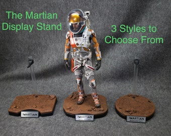 以下が含まれることがあります： 火星人アクションフィギュア用のディスプレイスタンドが3種類あります。各スタンドは、茶色の岩の表面と黒いベースを持っています。ベースには、「火星人」と「マーク・ワトニー」の文字が印刷されています。スタンドは透明なプラスチック製で、上部に黒い金属製のフックが付いています。