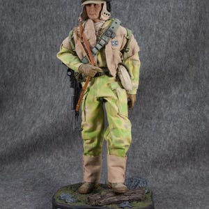May include: A detailed action figure of a Rebel Commando from Star Wars. The figure is wearing a green and brown camouflage uniform, a helmet, and carrying a blaster rifle. The figure is standing on a base with a Star Wars logo and the words "Rebel Commando".