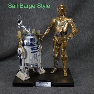 May include: A gold-colored C-3PO Star Wars action figure stands next to a white and blue R2-D2 action figure. Both figures are on a black base with the words "STAR WARS RETURN OF THE JEDI R2-D2 & C-3PO" printed on it.