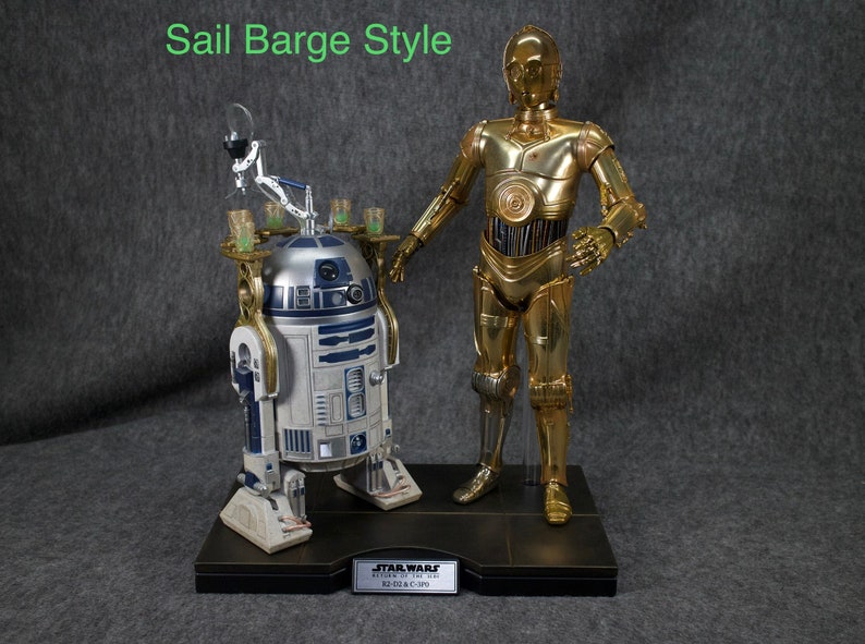 May include: A gold-colored C-3PO Star Wars action figure stands next to a white and blue R2-D2 action figure. Both figures are on a black base with the words "STAR WARS RETURN OF THE JEDI R2-D2 & C-3PO" printed on it.