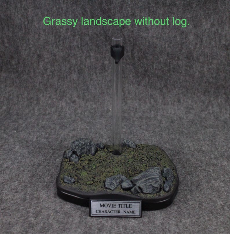 May include: A black plastic display stand with a clear acrylic rod. The base is designed to look like a grassy landscape with small rocks. The stand has a black label with the text "MOVIE TITLE" and "CHARACTER NAME".