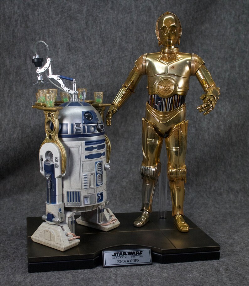 May include: A gold-colored C-3PO Star Wars action figure stands next to a white and blue R2-D2 action figure. Both figures are on a black base with a silver plaque that reads "Star Wars Return of the Jedi R2-D2 & C-3PO".