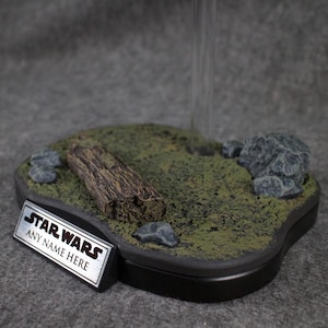 May include: A black display base with a green mossy surface, a log, and rocks. The base has a silver plaque with the text "STAR WARS ANY NAME HERE".