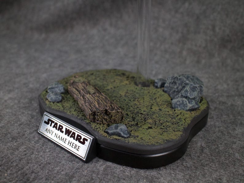 May include: A black display base with a green mossy surface, a log, and rocks. The base has a silver plaque with the text "STAR WARS ANY NAME HERE".