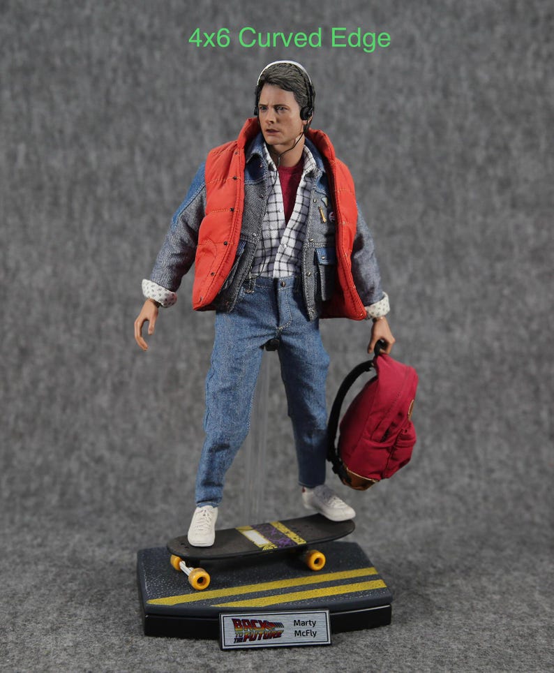 K&ouml;nnte beinhalten: Eine Figur tr&auml;gt eine rote Weste, eine blaue Jeansjacke und eine blaue Jeans. Sie h&auml;lt einen roten Rucksack und steht auf einem Skateboard. Die Figur tr&auml;gt ein Headset und hat braunes Haar. Das Skateboard hat gelbe R&auml;der und ein schwarzes Deck. Die Figur steht auf einem schwarzen Sockel mit den Worten "Zur&uuml;ck in die Zukunft" und "Marty McFly" darauf.