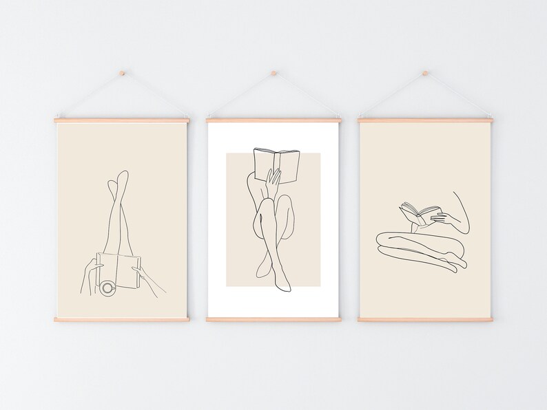 May include: Three minimalist line art prints featuring a person reading a book in different poses. The prints are framed with a light wood frame and hung on a white wall.