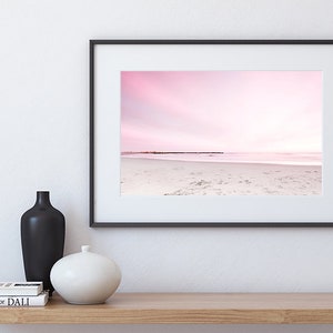 May include: A framed photograph of a pink and white beach scene with a horizon line and a row of wooden posts in the distance.