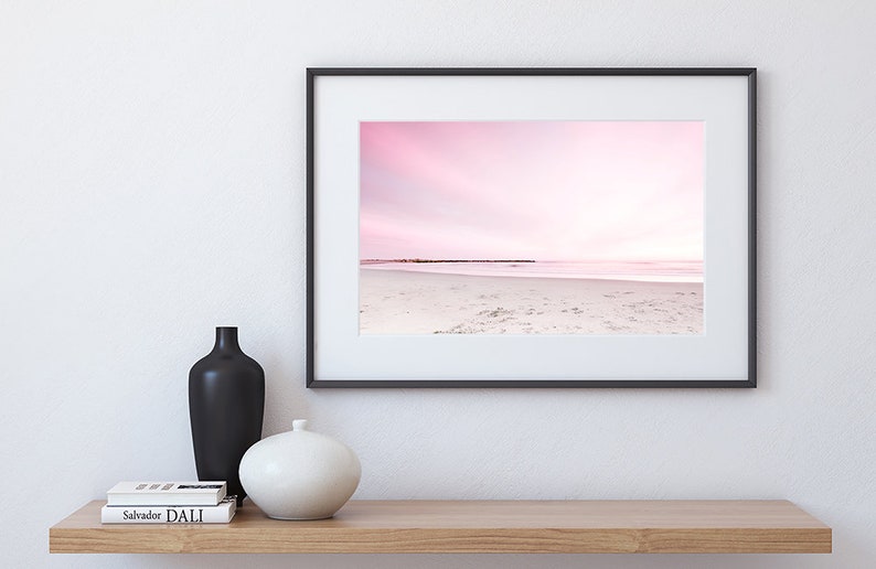 May include: A framed photograph of a pink and white beach scene with a horizon line and a row of wooden posts in the distance.