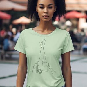 Op de afbeelding: Een lichtgroen T-shirt met een lijntekening van benen die uit een boek steken.