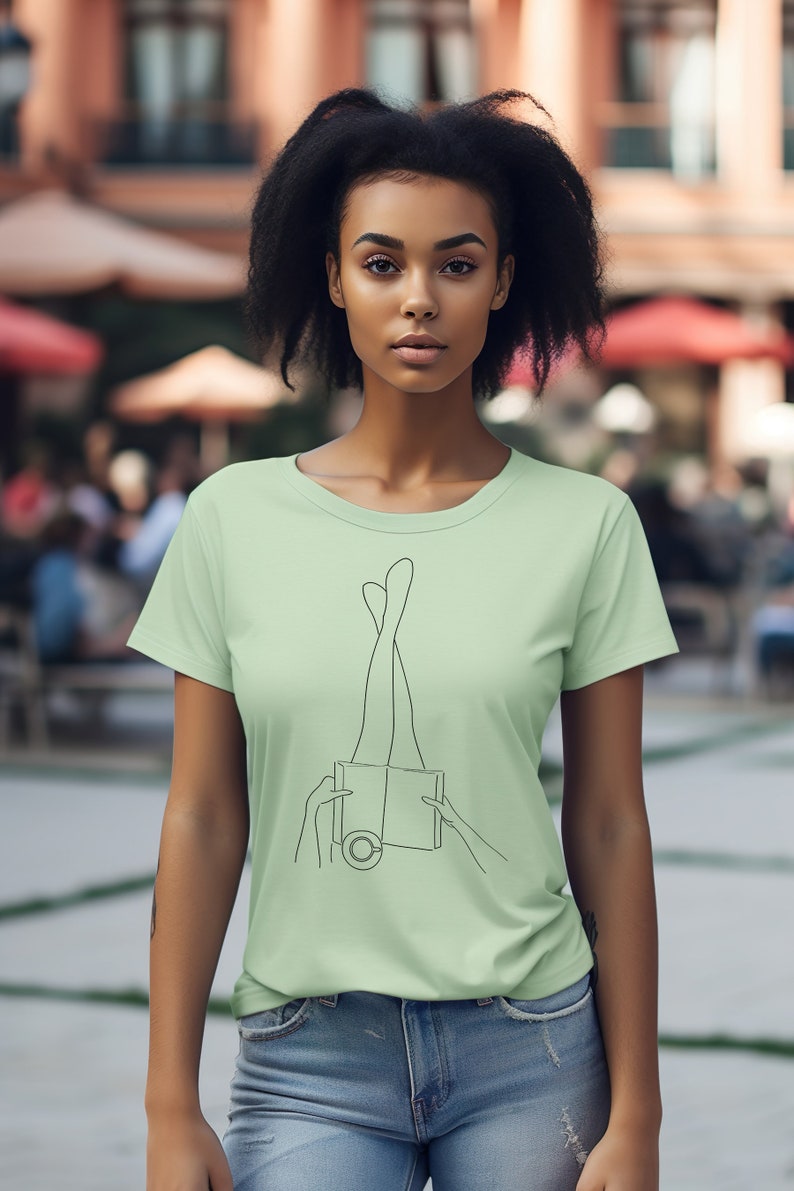 Op de afbeelding: Een lichtgroen T-shirt met een lijntekening van benen die uit een boek steken.