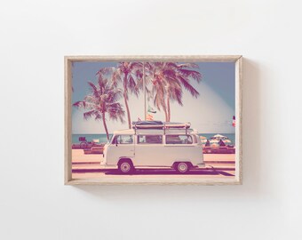 May include: A white vintage van with a surfboard on the roof parked on a beach with palm trees in the background.