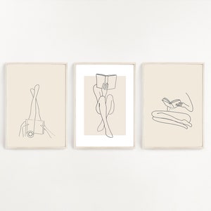 May include: Three minimalist line art prints featuring figures reading books. The prints are framed in a light wood frame and have a cream background.