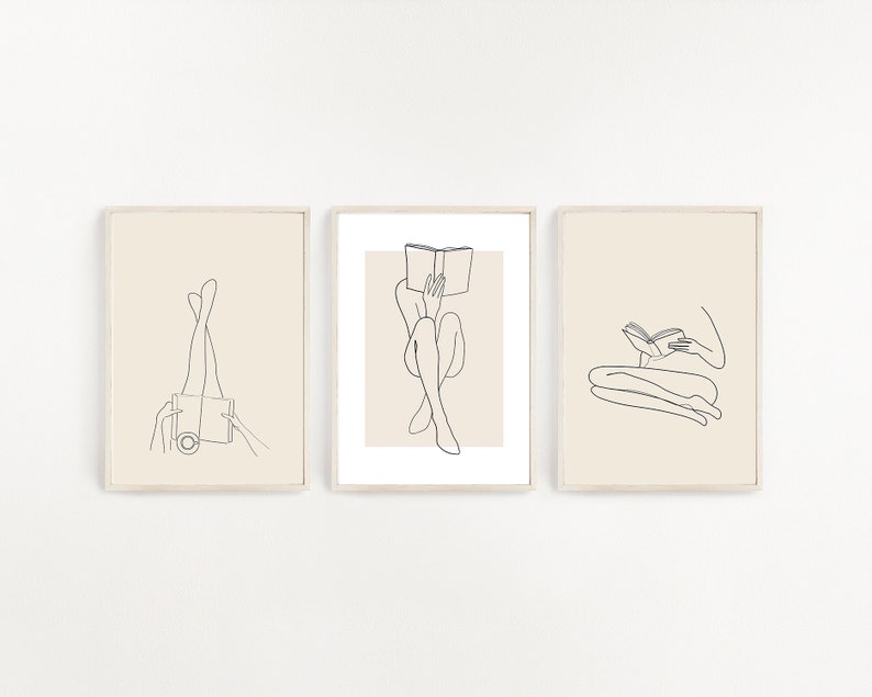 May include: Three minimalist line art prints featuring figures reading books. The prints are framed in a light wood frame and have a cream background.