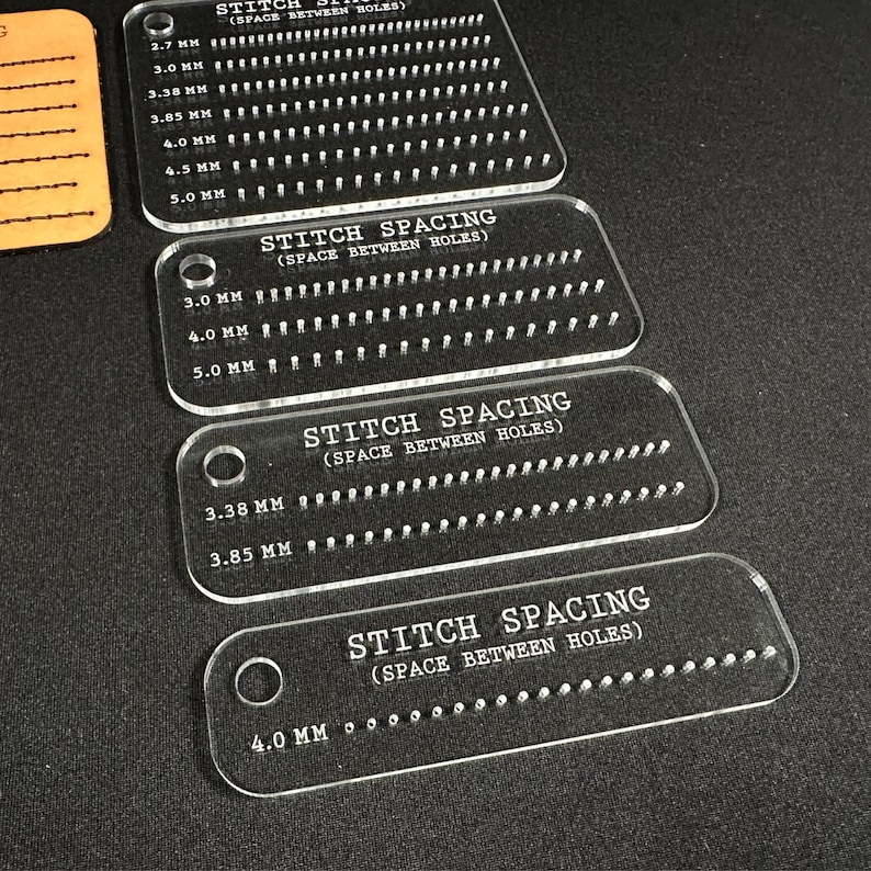 K&ouml;nnte beinhalten: Transparente Stichabstand-F&uuml;hrungen aus Acryl mit verschiedenen Lochabst&auml;nden in Millimetern. Die F&uuml;hrungen sind mit Messungen von 2,7 mm bis 5,0 mm beschriftet. Der Text "STITCH SPACING (SPACE BETWEEN HOLES)" ist aufgedruckt.