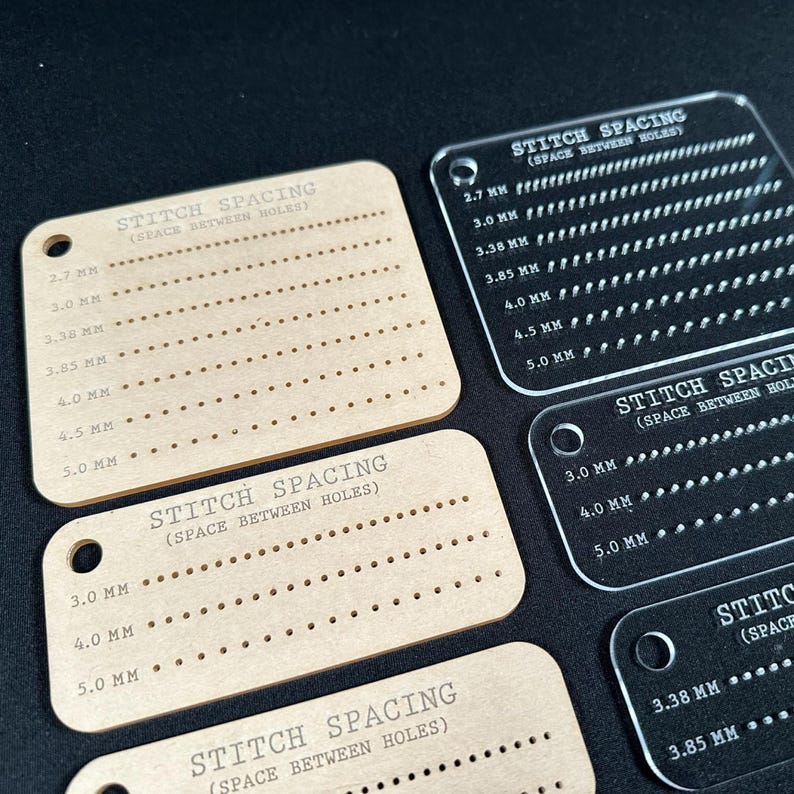 K&ouml;nnte beinhalten: Eine Sammlung von Stichabstand-F&uuml;hrungen. Die F&uuml;hrungen bestehen aus transparentem und hellbraunem Acryl. Jede F&uuml;hrung hat eine Reihe von gleichm&auml;&szlig;ig verteilten L&ouml;chern und ist mit dem Stichabstand in Millimetern beschriftet. Der Text "STITCH SPACING (SPACE BETWEEN HOLES)" ist auf jeder F&uuml;hrung aufgedruckt.