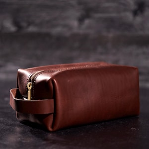 May include: A brown leather travel bag with a gold zipper and a leather handle.