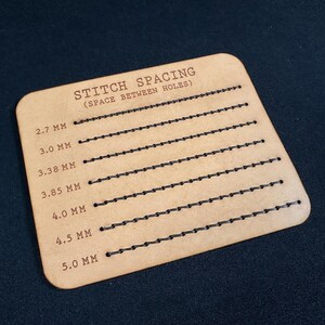 K&ouml;nnte beinhalten: Ein hellbraunes Leder-Steppabstandswerkzeug mit dem Text "STITCH SPACING (SPACE BETWEEN HOLES)". Das Werkzeug hat mehrere Reihen von gleichm&auml;&szlig;ig verteilten L&ouml;chern, die jeweils mit einem Millimeterma&szlig; beschriftet sind, von 2,7 mm bis 5,0 mm.