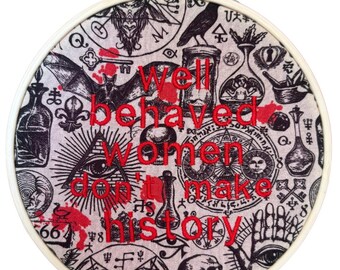 Puede incluir: Bastidor de bordado redondo con tela crema con símbolos ocultos negros y el texto rojo "Well behaved women don't make history." El diseño incluye un cuervo, un murciélago, un ojo y una calavera.