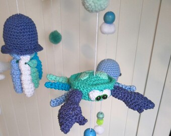 May include: A crocheted baby mobile featuring a blue jellyfish, a green crab, and blue and green pom-poms.