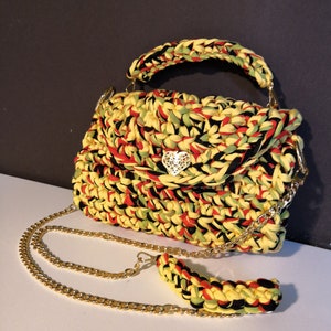May include: A small yellow, red and black crocheted handbag with a gold chain strap and a heart-shaped clasp.