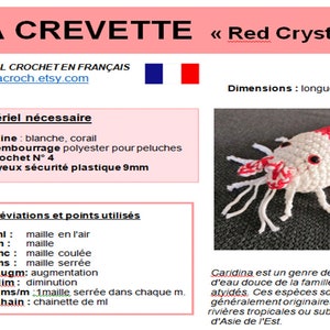 K&ouml;nnte beinhalten: Geh&auml;kelte Garnele, haupts&auml;chlich wei&szlig; mit roten Akzenten, mit schwarzen Sicherheitsaugen und langen wei&szlig;en Antennen. Der Text &bdquo;LA CREVETTE Red Crystal&ldquo; ist &uuml;ber dem Bild zu sehen, zusammen mit franz&ouml;sischem Text und einem H&auml;kel-Tutorial.