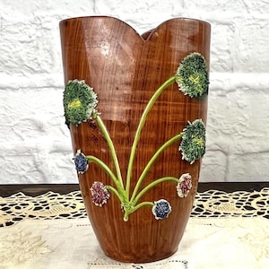 May include: A tall, brown vase with a unique, asymmetrical top. The vase is adorned with green, blue, and red floral accents. The vase has a wood-grain texture and is suitable for displaying flowers or as a decorative piece.