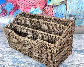 May include: A rectangular brown woven seagrass basket featuring three distinct interior compartments separated by vertical dividers. The basket has a textured, braided surface and an open top design, providing organized storage space for various items.
