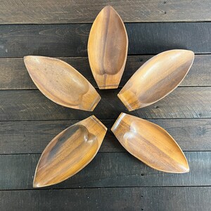 Pode incluir: Cinco tigelas de madeira em forma de folha, dispostas em forma de estrela sobre uma superfície de madeira escura.