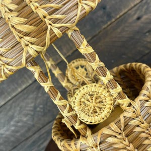 May include: A decorative hot air balloon sculpture crafted from light brown pine needles and natural raffia. The structure features a woven basket base, a spherical upper section, and vertical supports connected by small, circular woven accents.