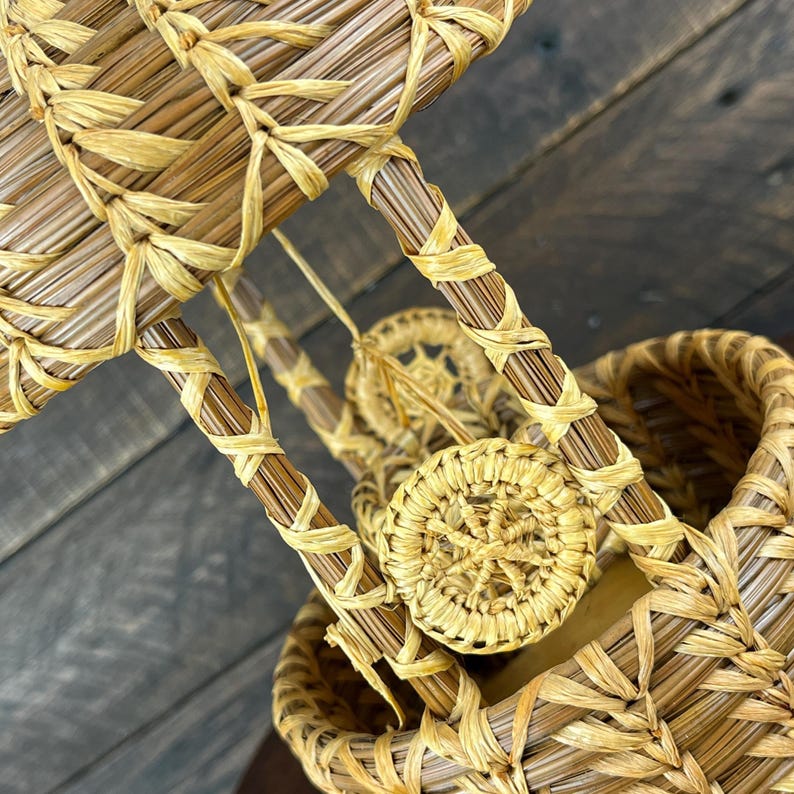 May include: A decorative hot air balloon sculpture crafted from light brown pine needles and natural raffia. The structure features a woven basket base, a spherical upper section, and vertical supports connected by small, circular woven accents.