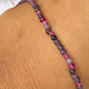 Op de afbeelding: Een delicate armband bestaande uit kleine, ronde kralen in tinten roze, paars en grijs. De armband wordt om een pols gedragen, waarbij de subtiele kleurvariaties van de kralen te zien zijn. De kralen zijn ongeveer 0,25 cm in diameter.