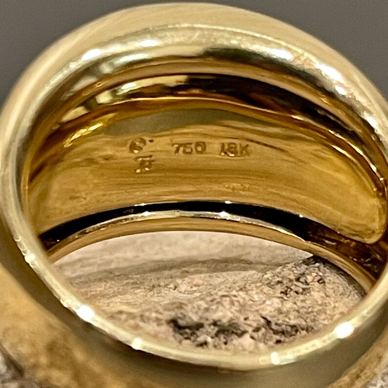 May include: Close-up of the inside of a gold ring with the inscription "750 18K" on the band.