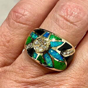 May include: A gold ring with a black, green, and blue opal inlay. The center of the ring features a cluster of small diamonds.