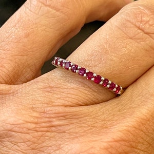 May include: A silver band ring with a row of small, red ruby stones.
