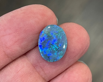 May include: A blue and green opal cabochon with a swirling pattern. The opal is oval shaped and has a high polish.