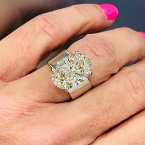 May include: A large, oval-shaped diamond ring with a thick, white gold band. The ring is set with two large, oval-shaped diamonds.