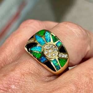 May include: A gold ring with a black, green, and blue opal design. The center of the ring features a cluster of small diamonds.