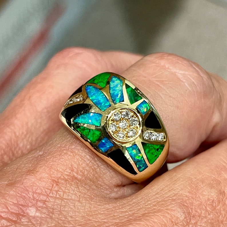 May include: A gold ring with a black, green, and blue opal design. The center of the ring features a cluster of small diamonds.
