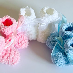 May include: Three pairs of baby booties in pink, white, and blue. Each pair is made of soft, fluffy material and tied with a satin ribbon. The pink booties have pink ribbons, the white have white, and the blue have blue.