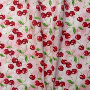May include: Pink fabric with a repeating pattern of red cherries with green stems and leaves.