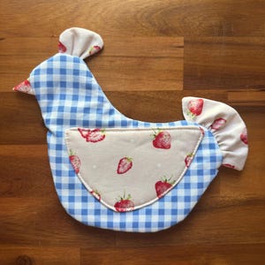 May include: A chicken-shaped fabric item featuring a blue and white gingham pattern on the body, head, and tail. A cream-colored wing patch is centered on the side, decorated with a repeating red strawberry print and small white dots.