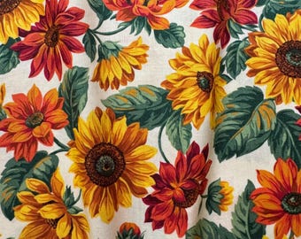 May include: A white fabric with a repeating pattern of red, orange, and yellow sunflowers. The sunflowers have dark brown centers and are surrounded by green leaves.