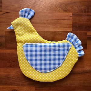 May include: A fabric chicken-shaped ornament featuring a yellow body with white polka dots, a blue and white gingham wing, a blue and white gingham comb on the head, and a blue and white gingham tail. The item is constructed from quilted textile.