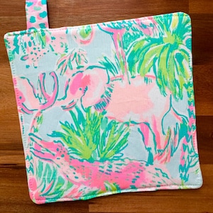 May include: Square, light blue pot holder with a colorful tropical print featuring pink elephants, green palm trees, and other flora. A small pink and blue patterned loop is attached to the top corner. The pot holder is edged with white stitching.